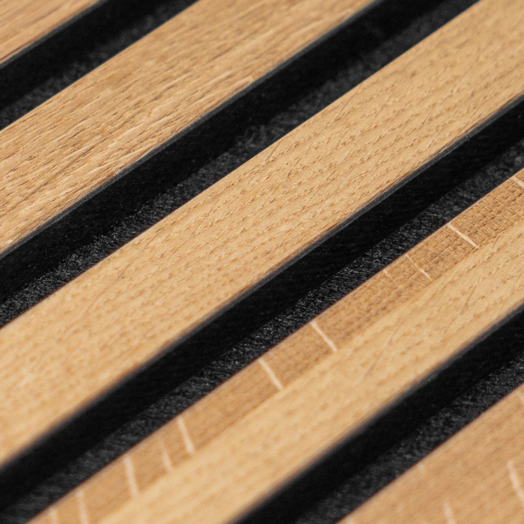 Zbliżenie produktu WoodUpp: równoległe, jasne drewniane listwy dębowe ułożone naprzemiennie z czarnymi, miękkimi paskami filcowymi. Elegancki panel-organizer WoodUpp z gładkimi, frezowanymi krawędziami, widocznymi słojami i precyzyjnymi szczelinami, przeznaczony do wykończeń biurka lub uporządkowania akcesoriów. Zdjęcie pokazuje naturalną fakturę drewna i kontrast czerni, podkreślający designerski charakter produktu.