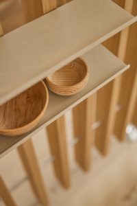 Zdjęcie przedstawia półkę WoodUpp z beżową, minimalistyczną półką o matowym wykończeniu zamocowaną na pionowych, jasnych drewnianych lamelach. Na półce stoją dwie okrągłe, ręcznie wykończone miseczki WoodUpp z widocznym, naturalnym usłojeniem — większa i mniejsza, w ciepłej tonacji beżów i brązów, z delikatnymi cieniami.